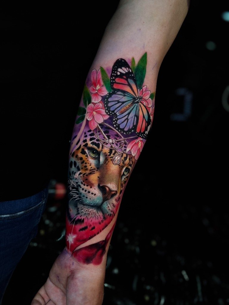 Tatuaje a color de jaguar con flores y mariposa en el antebrazo