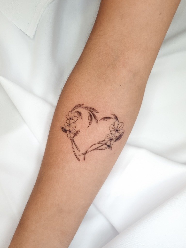 Tatuaje fine line de corazón hecho de ramas y flores en el antebrazo
