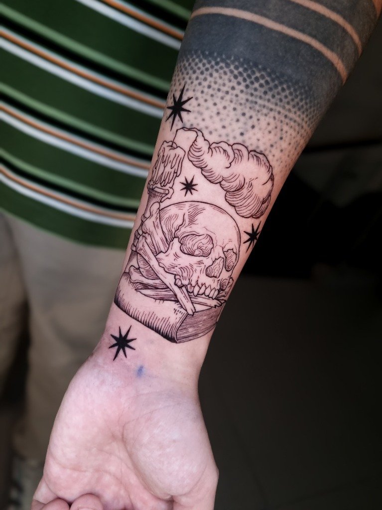 Tatuaje fine line de cráneo sobre libro y vela con humo en el antebrazo