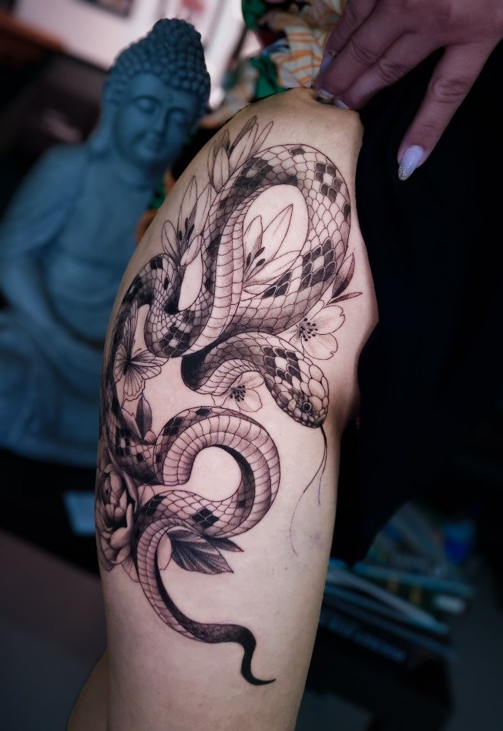 Tatuaje en sombras de serpiente enroscada en flores en el muslo